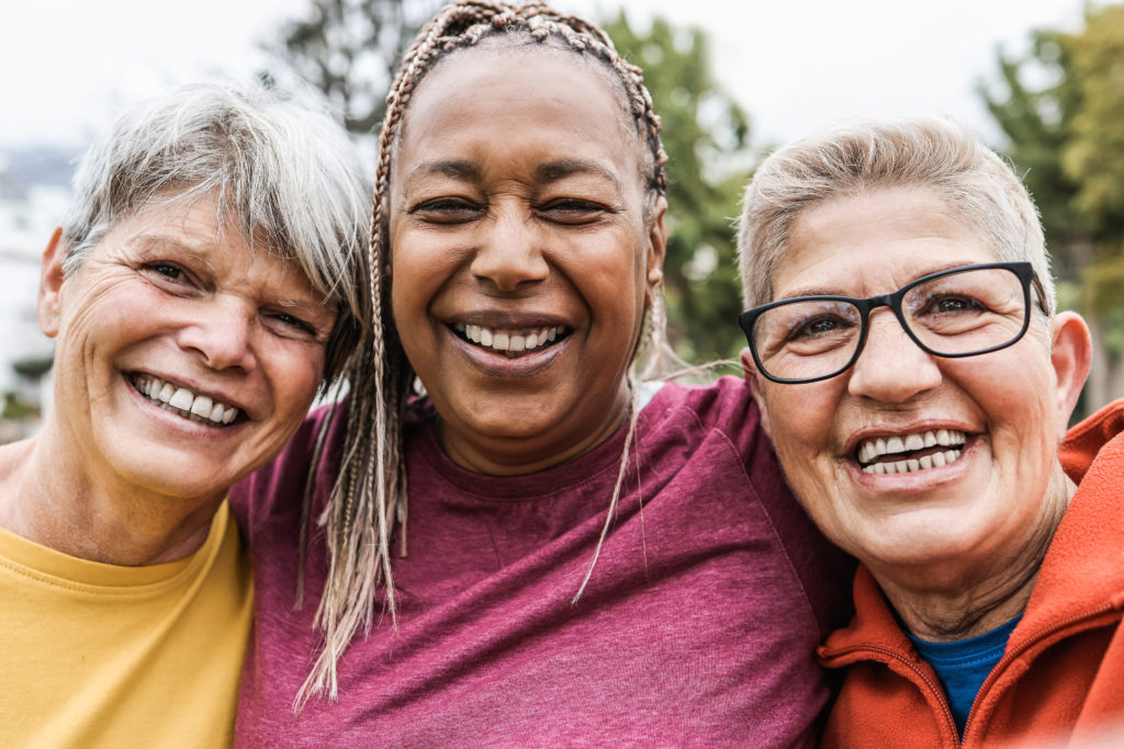 Three older women smiling, gathered together after exercising outdoors. Focal point on Black woman's face.