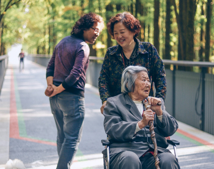Two older women on a bridge, one woman is pushing the other in a wheelchair. 